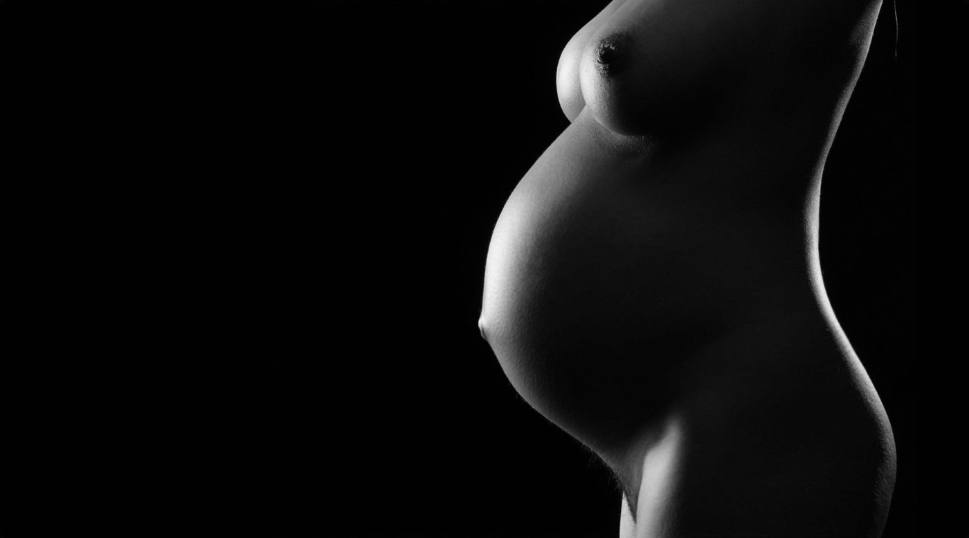 Halbakt einer schwangeren Frau mit Brust im studio vor dunklem Hintergrund