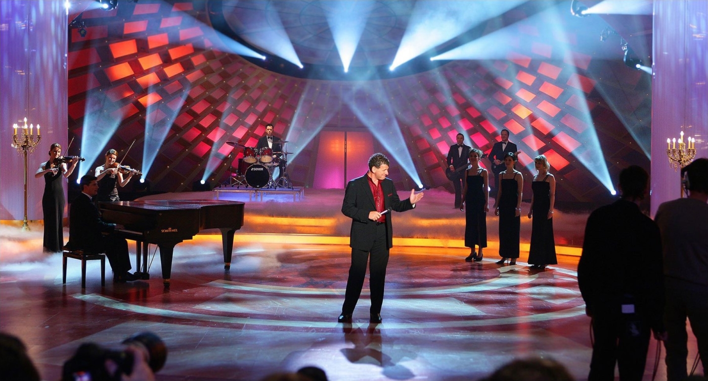 Klassischer Musikabend. Sänger auf der Bühne mit Chor und Pianisten im Hintergrund