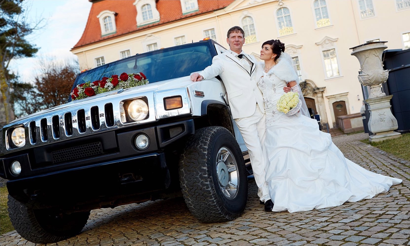 Mondänes Hochzeitspaar an ihren Hummer gelehnt im Hintergrund das Schloss Lichtenewalde