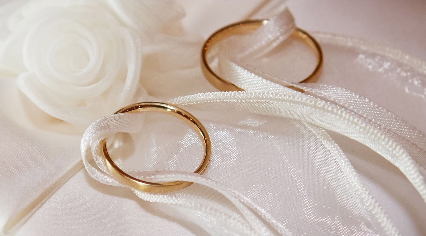Nahaufnahme der Eheringe auf weisser Seide mit Band verbunden
