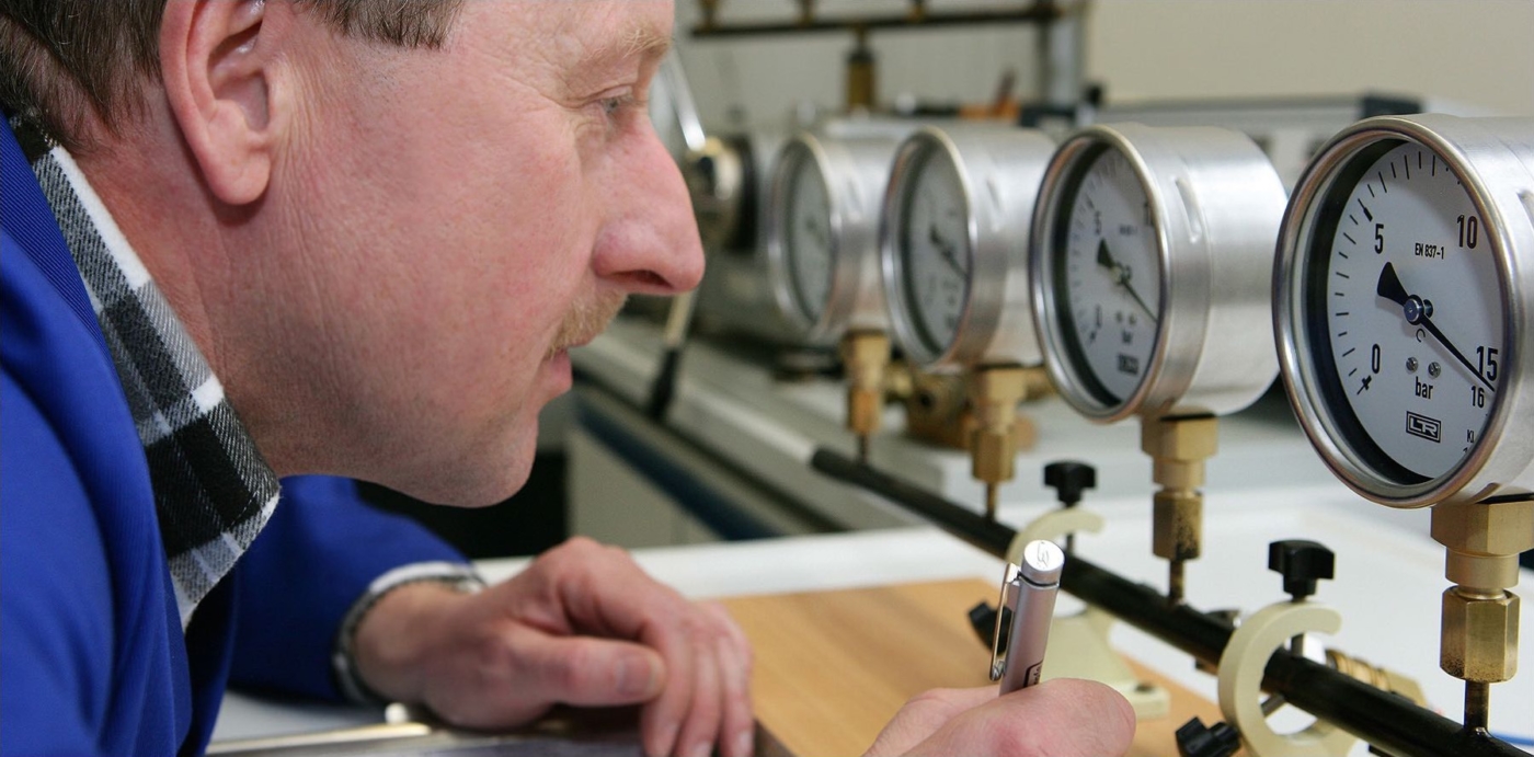 Nahaufnahme eines Mannes beim ablesen von Manometern in einer Messstation mit Stift in der Hand