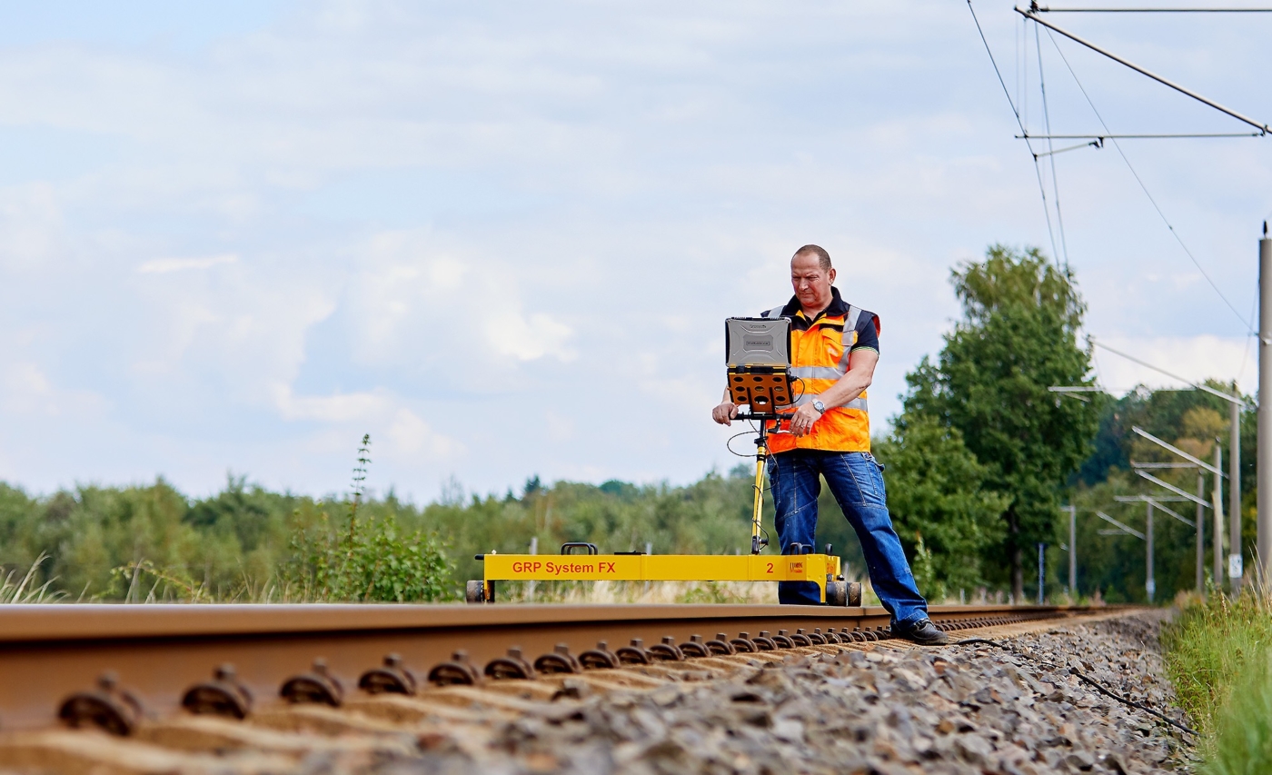 Arbeiter in Warnweste auf einem Gleisabschnitt beim Vermessen der Schienen in der Natur