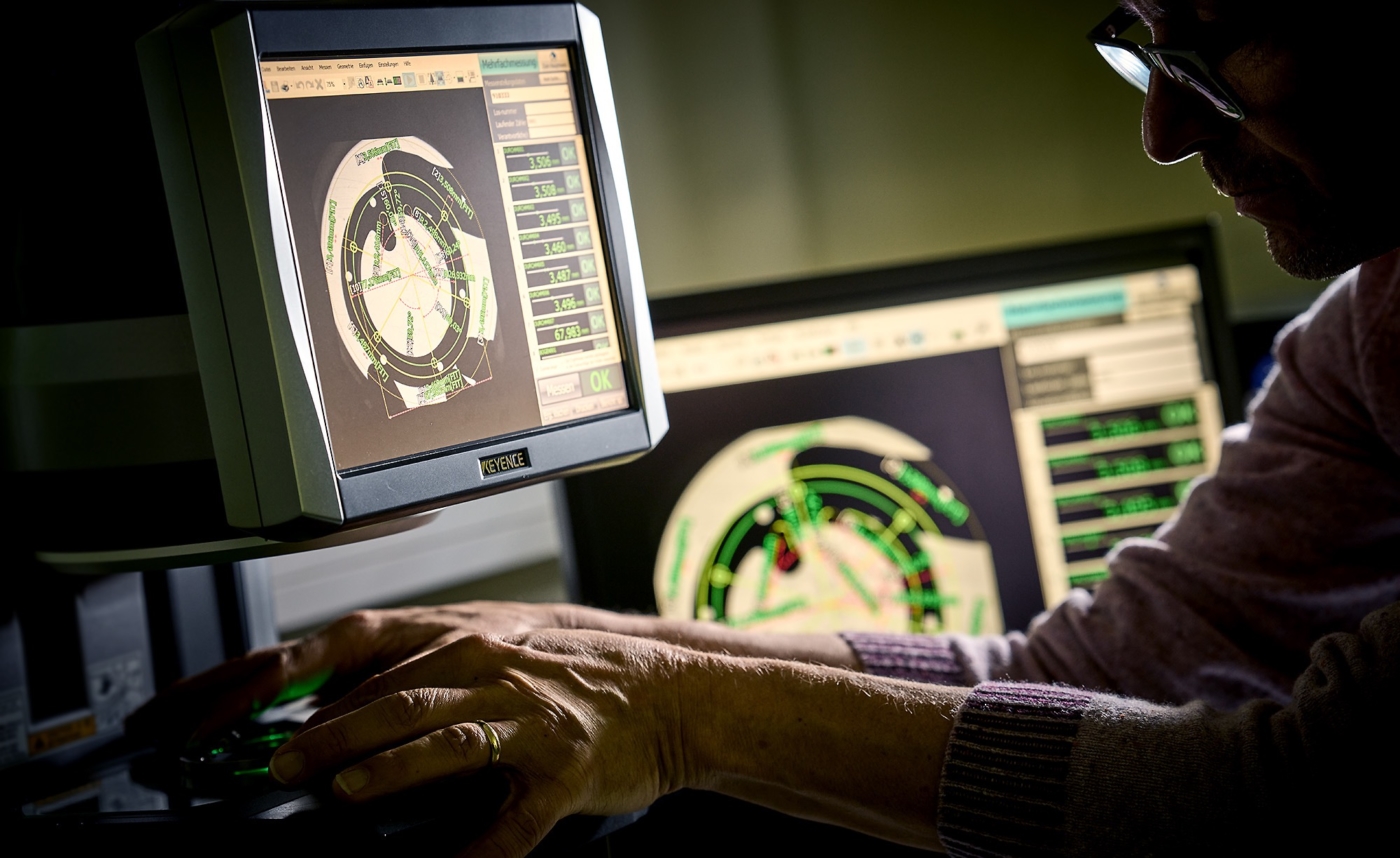 Qualitätstester an seinen Messbildschirm mit den Händen am Bauteil und mystischem Licht