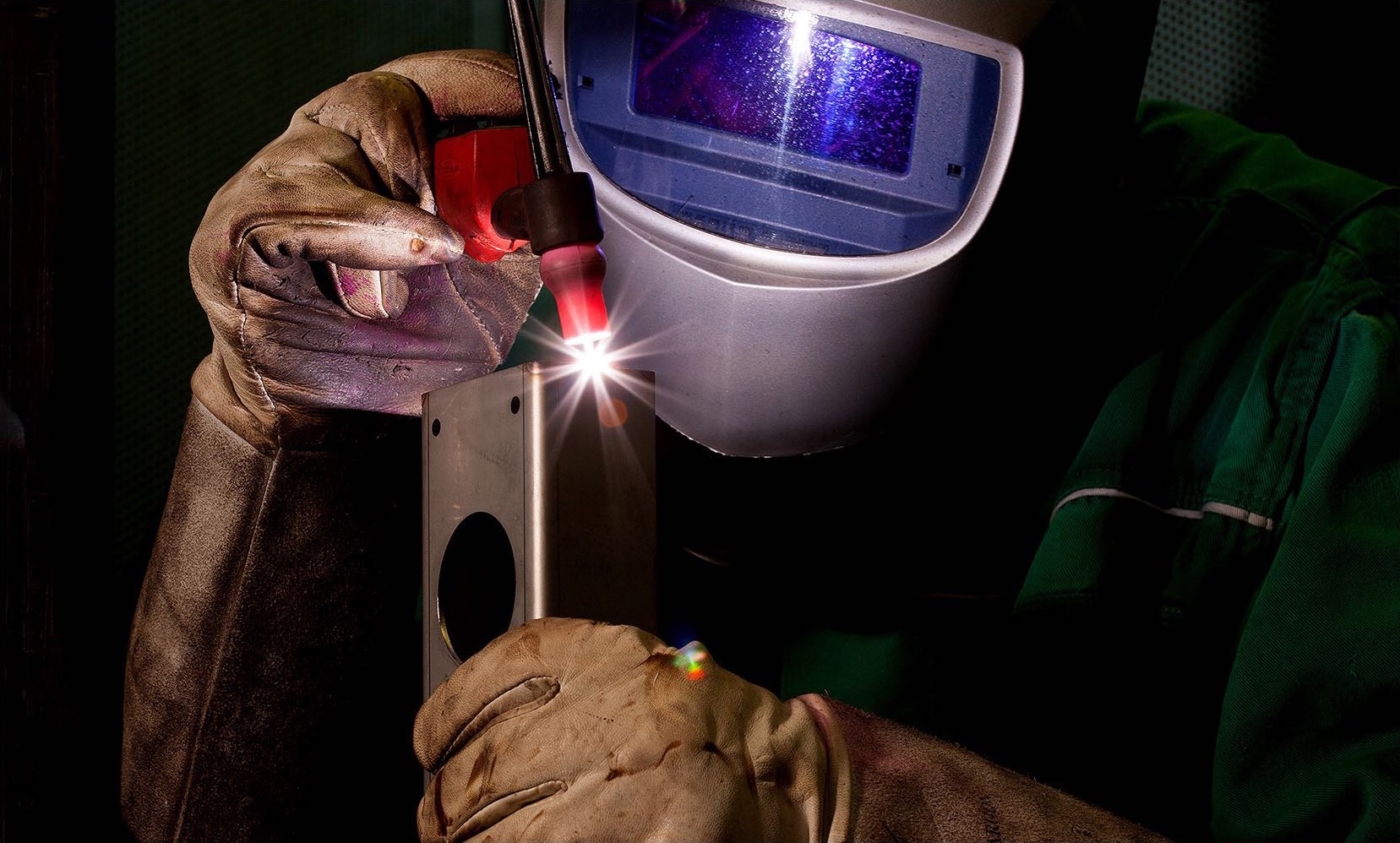 Elektro Schweisser, mit Brille und Handschuhen bei der Arbeit mit Bauteil in den Händen