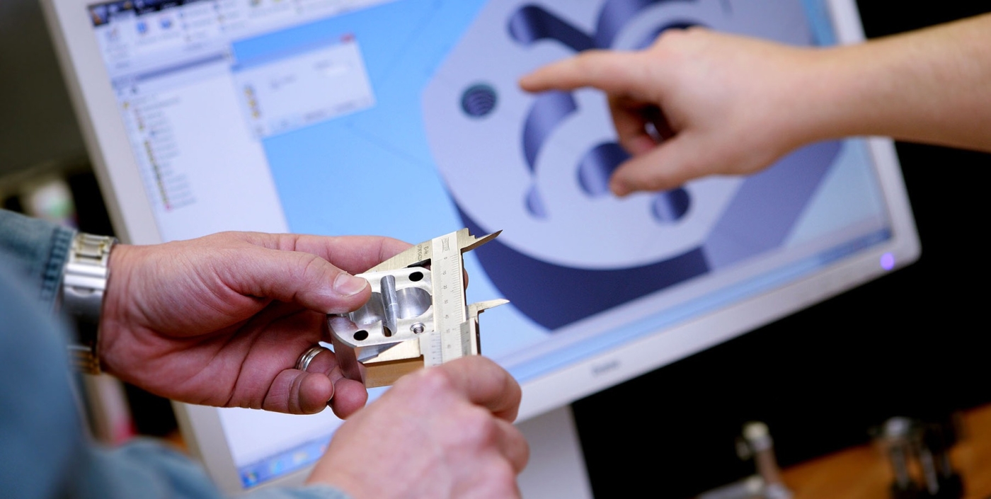 Ingenieur beinvermessen eines Bauteiles mit Schiebelehre im Hintergrund Bildschirm mit Konstruktionszeichnung