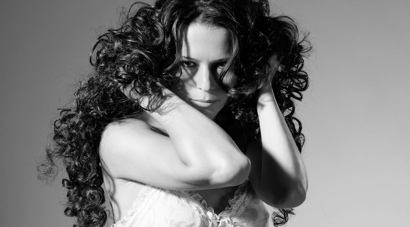 Portrait einer Frau mit viel gelocktem Haar und Händen in den Haaren